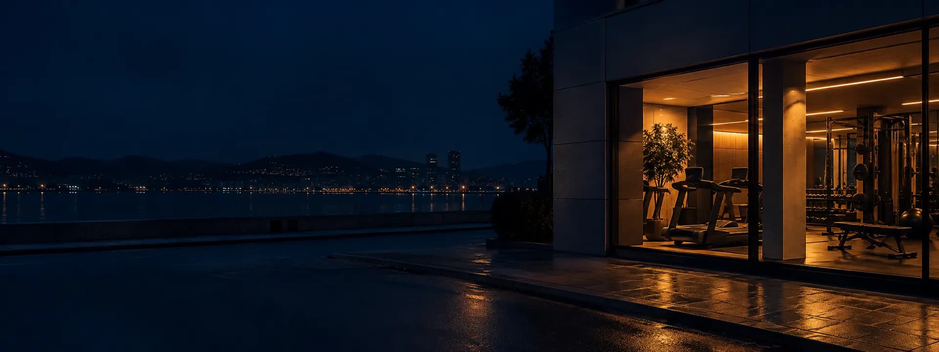Un gimnasio visto desde la calle de noche, con el ventanal iluminado y las máquinas dentro