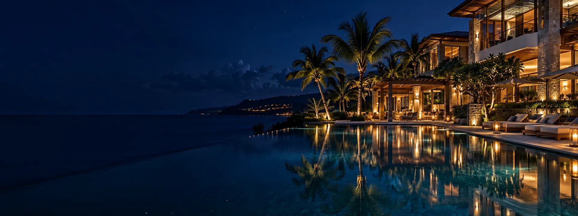 Un resort de lujo de noche, con la alberca iluminada y palmeras frente al mar