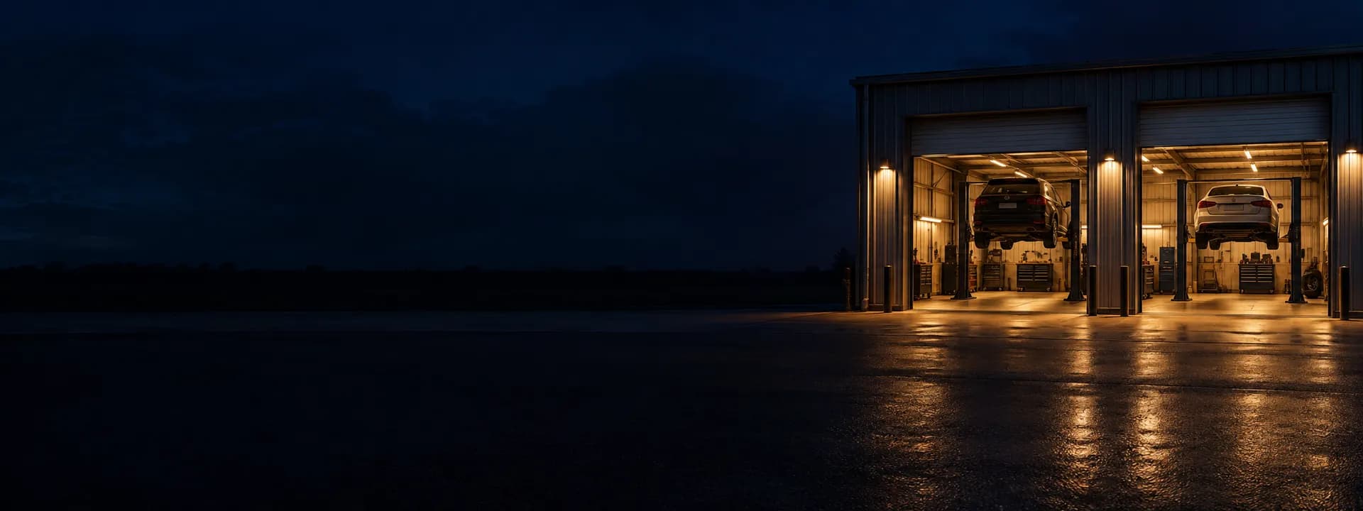 A repair shop's front at night with the doors up and cars on the lifts